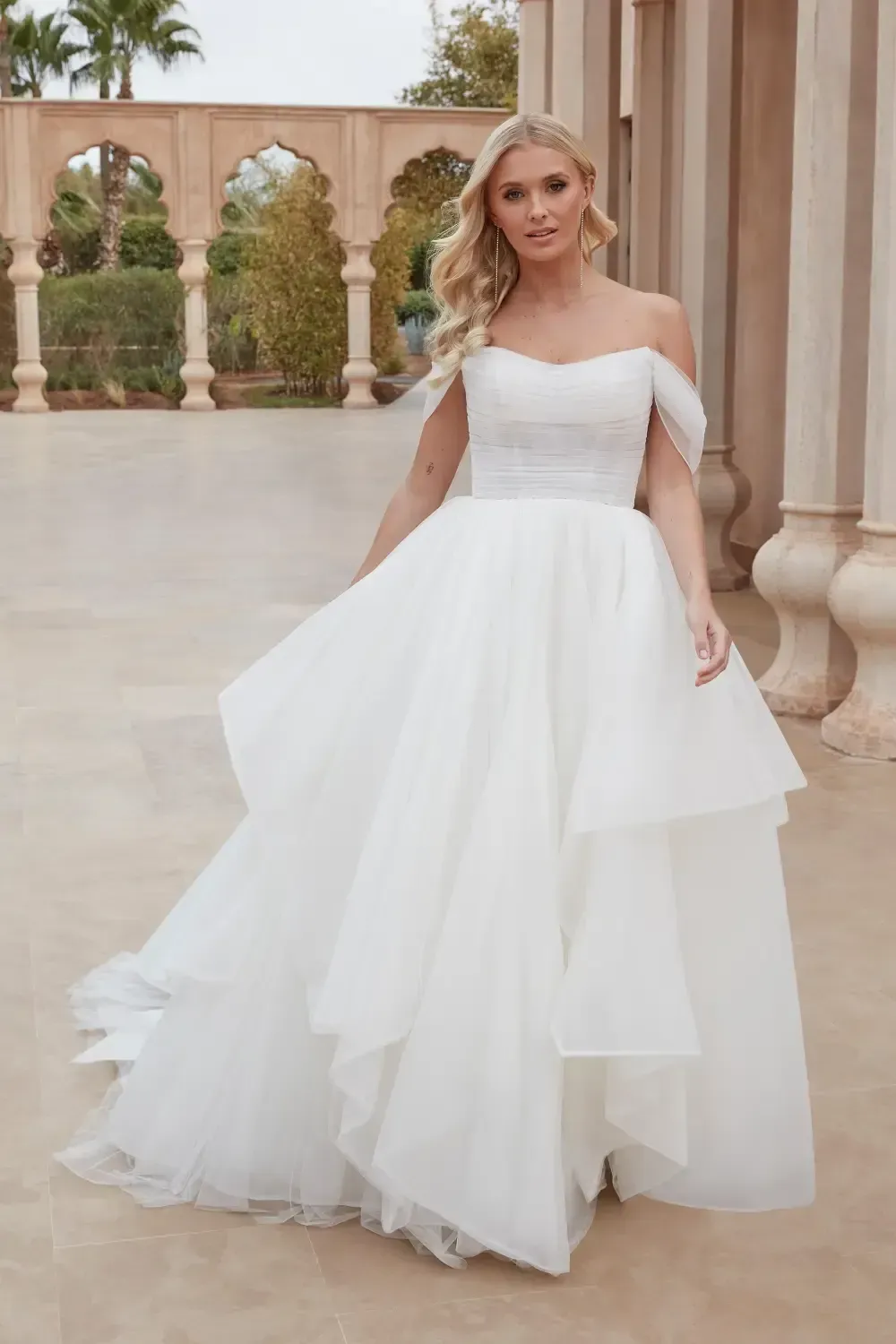 Woman in white off-shoulder wedding dress, standing outdoors.