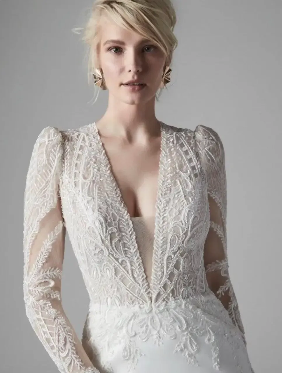 Woman in a white lace wedding dress with plunging neckline and long sleeves, posing.