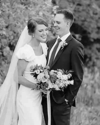 Couple embracing at sunset, groom kissing bride's cheek; dunes in background.