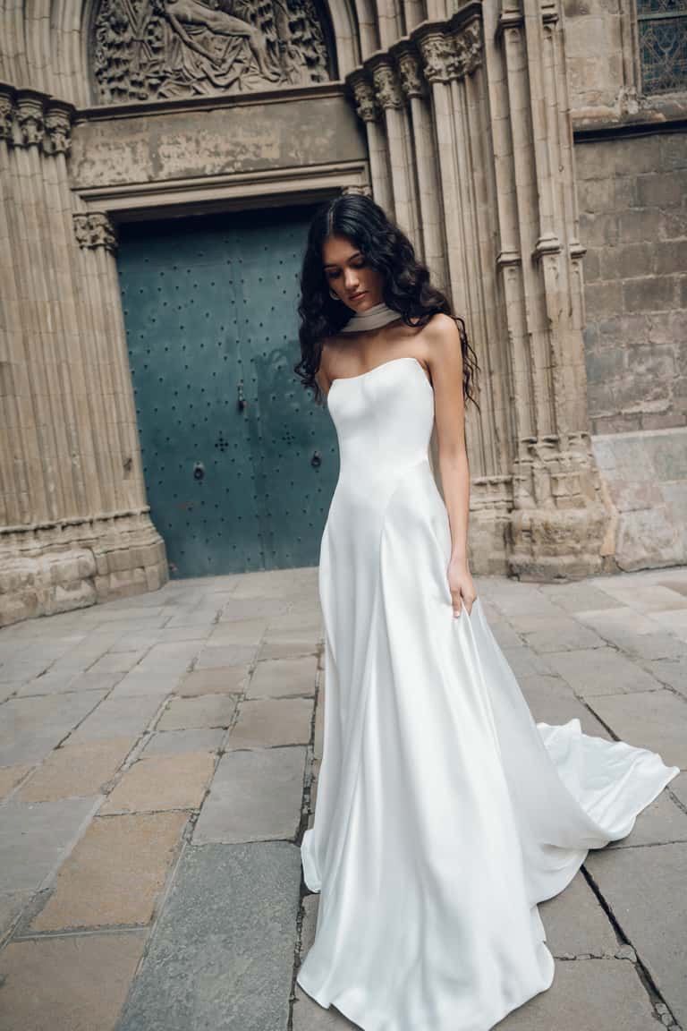 Woman in white strapless gown stands in front of a stone building with a large wooden door.