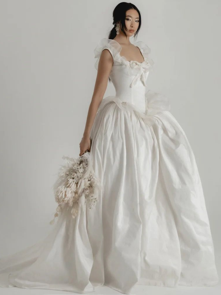 Woman in a white wedding gown, holding bouquet, posing against a white background.