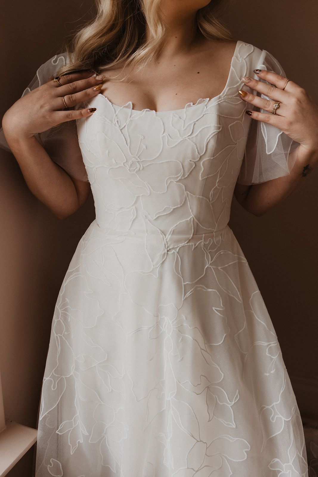 Woman in white lace dress, hands on chest. Beige background.