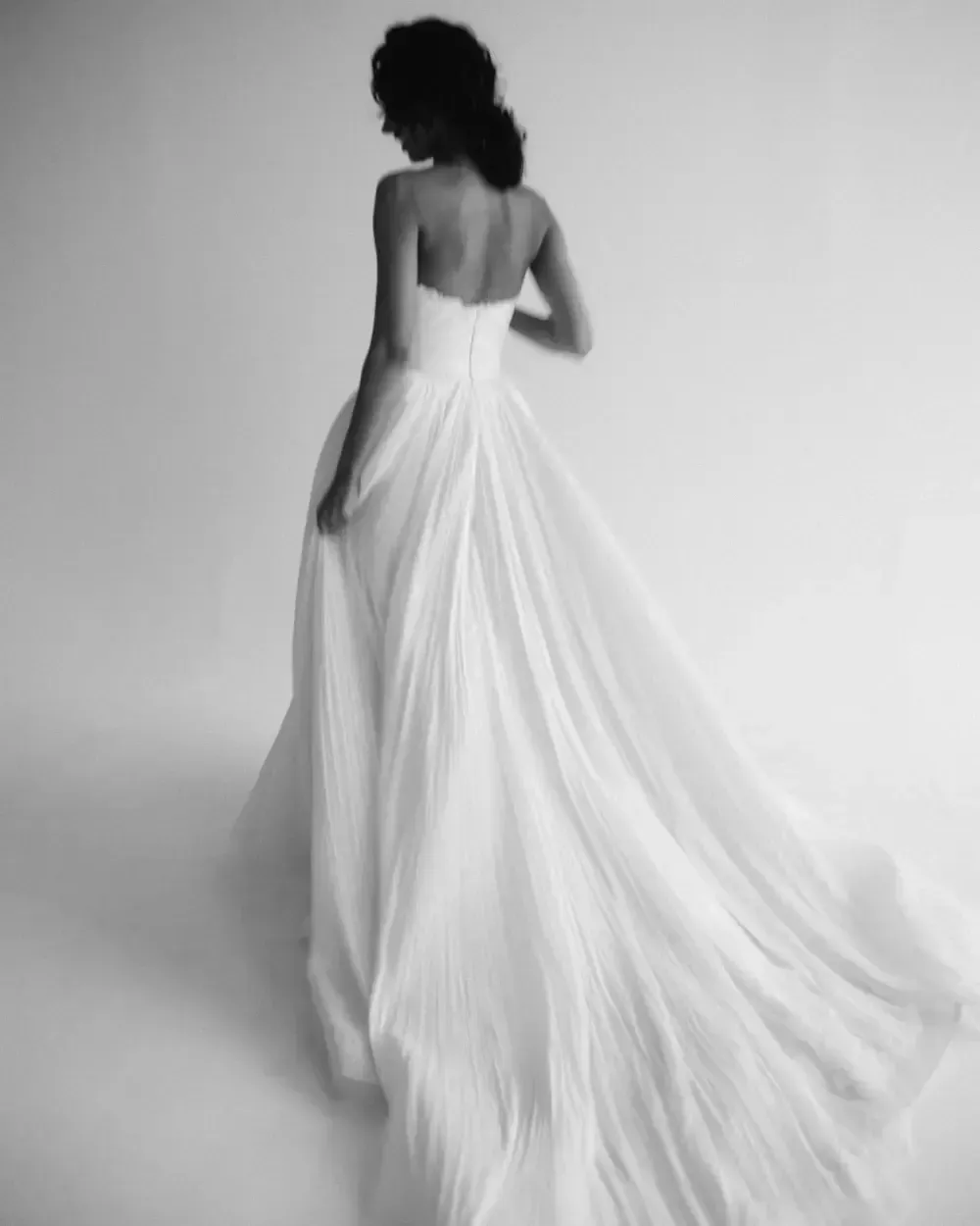 Woman in a white strapless gown, back to the camera, with a flowing train.