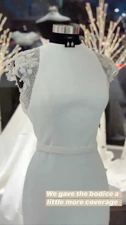 White wedding dress on a mannequin with beaded cap sleeves and a belted waist.