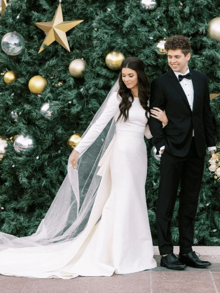 Couple posing in front of a Christmas tree; woman in wedding dress, man in tuxedo.
