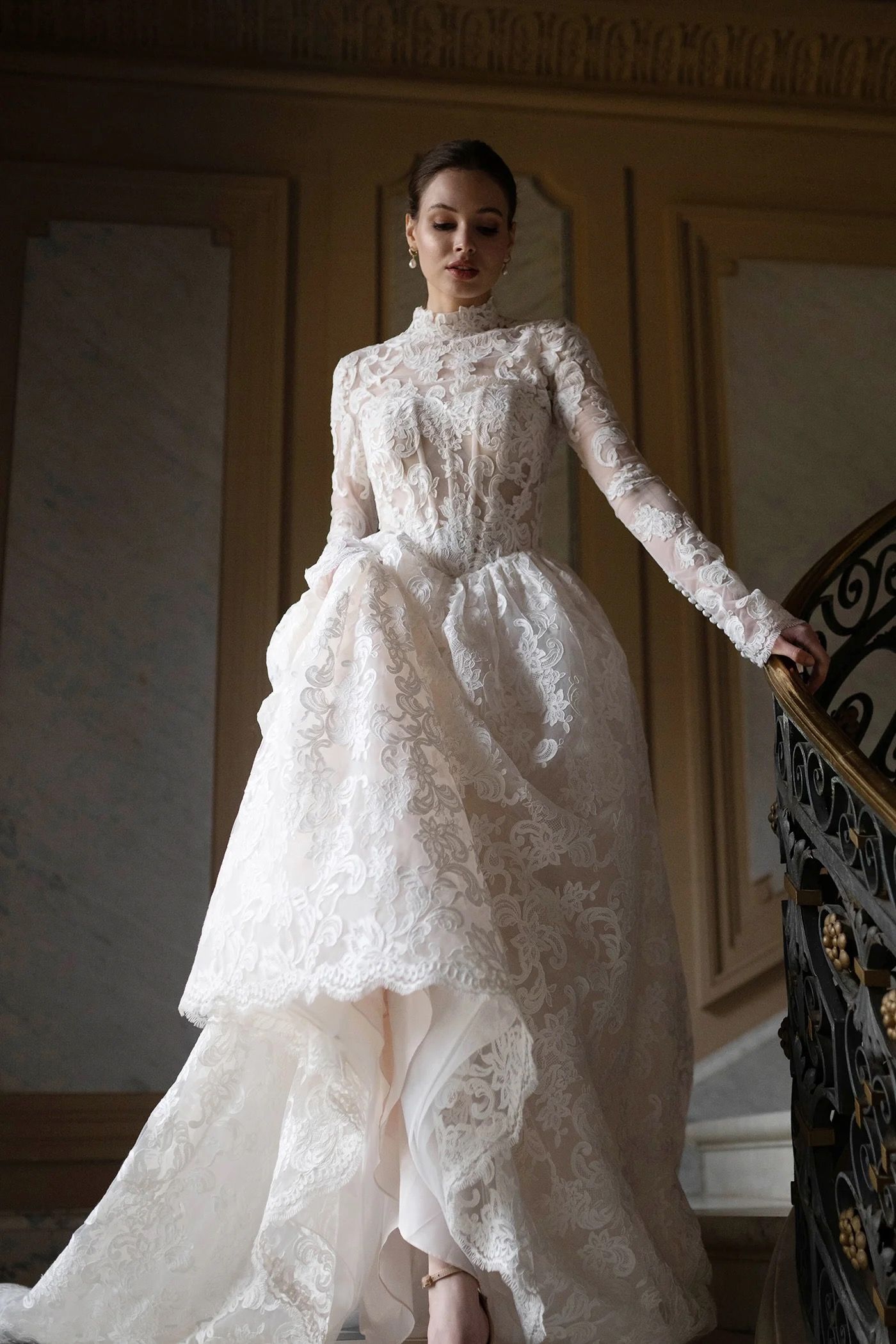 Woman in white lace gown on ornate staircase.