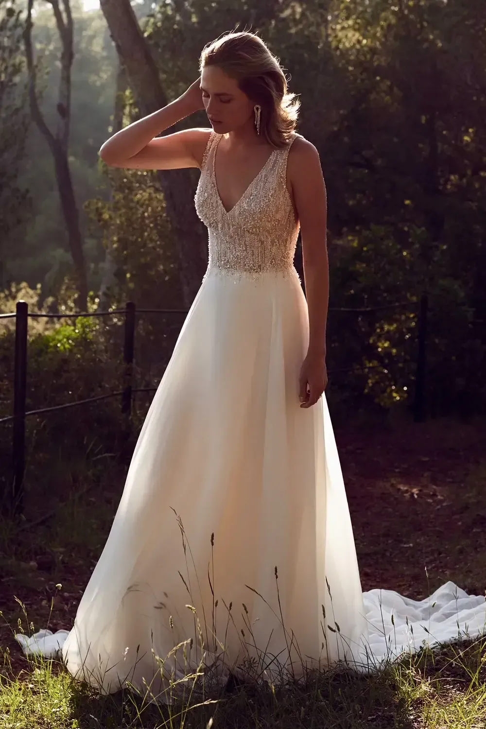 Woman in a wedding dress, beaded bodice and flowing skirt, outdoors in sunlight.