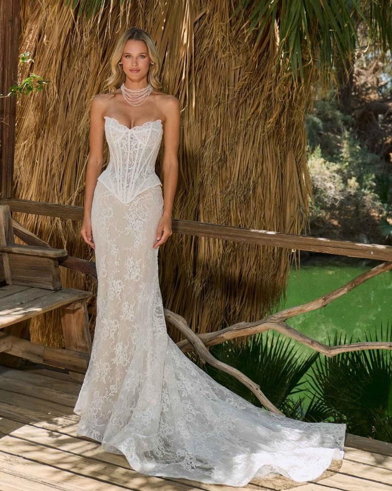 Woman in a white lace strapless wedding gown with a train, standing outdoors.