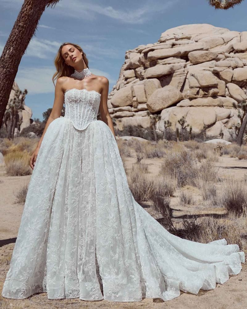 Woman in white strapless wedding gown with long train, posing in a desert landscape.