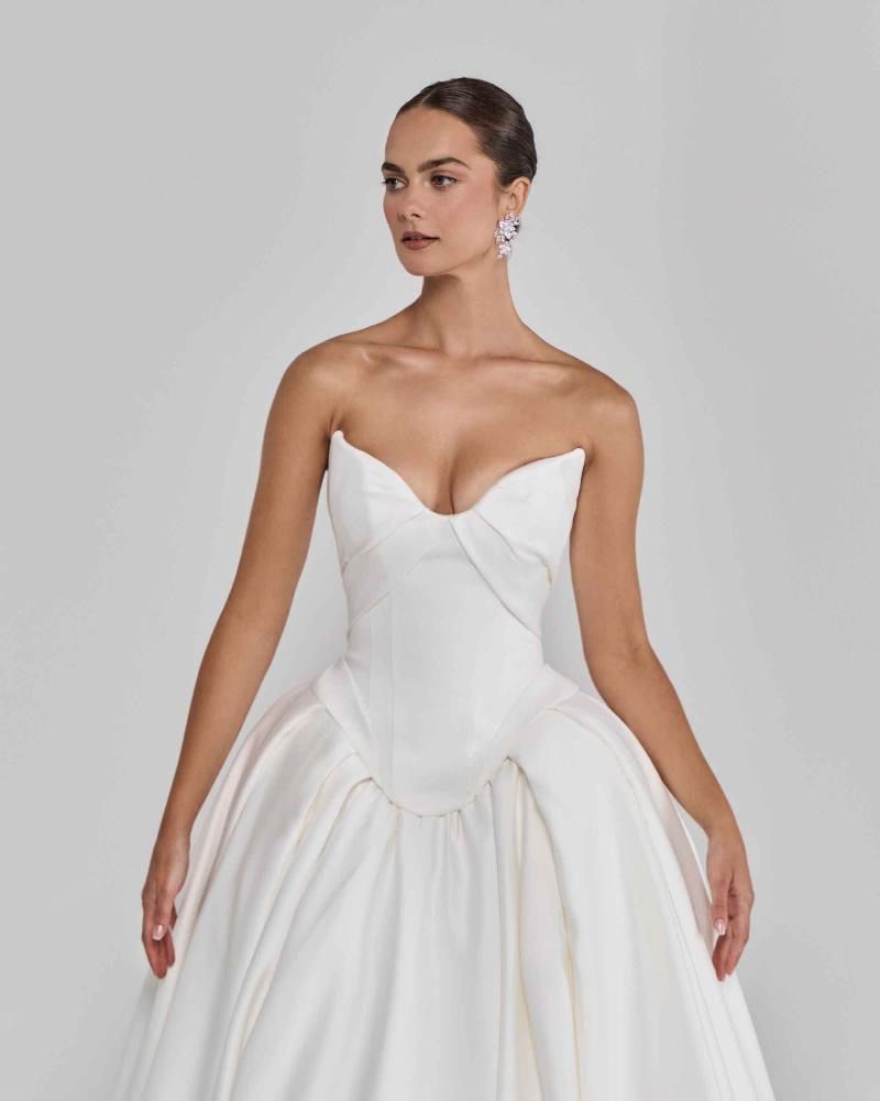 Woman in white strapless wedding gown, bustier bodice, full skirt. She is wearing earrings.