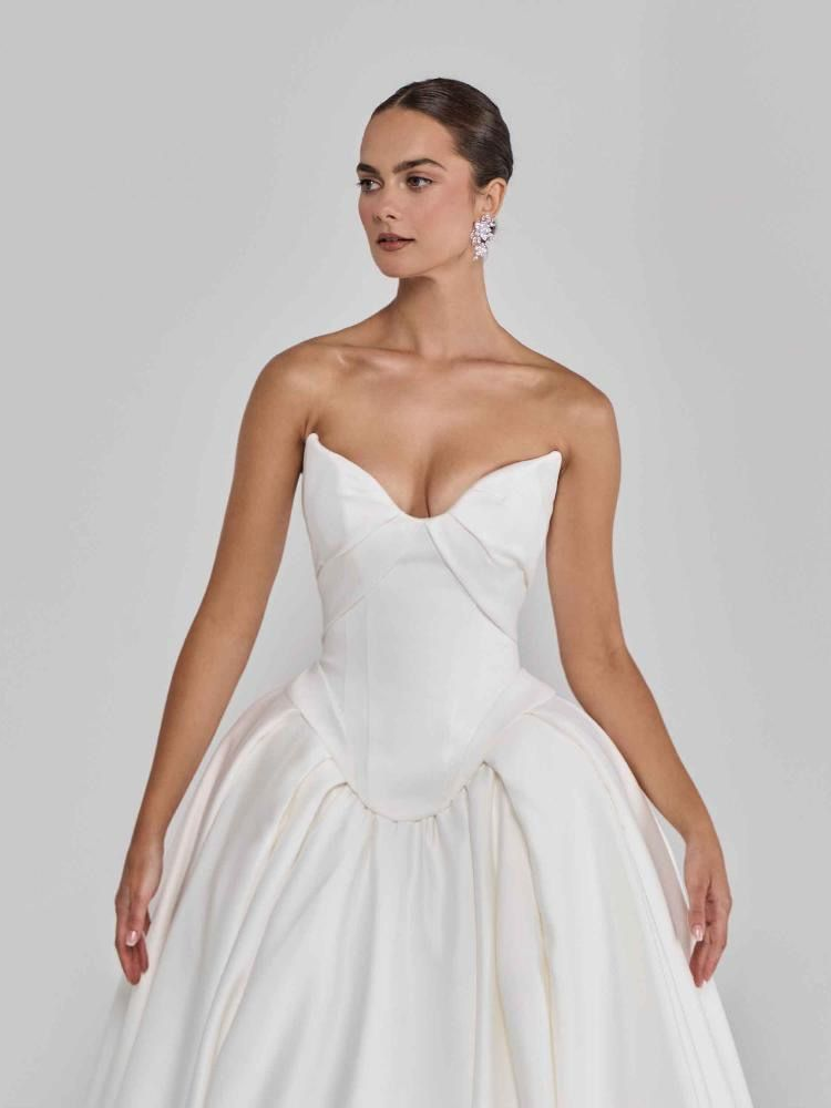 Woman in white strapless wedding gown, bustier bodice, full skirt. She is wearing earrings.