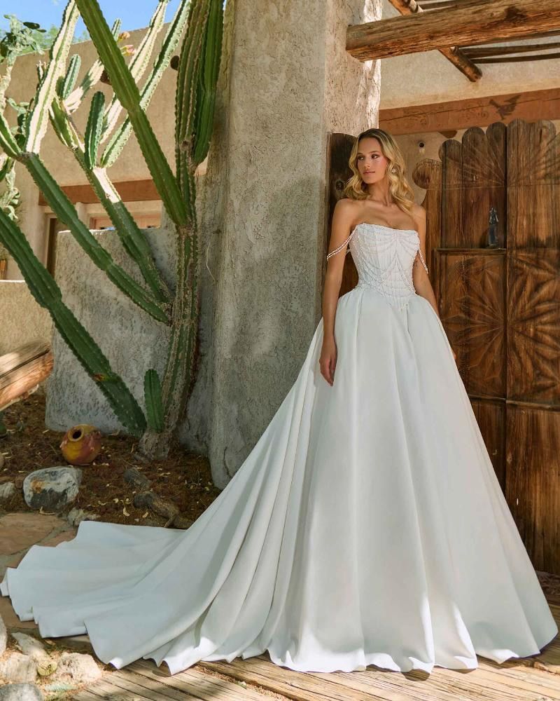 Woman in strapless white wedding dress with long train, standing near a cactus and wooden door.