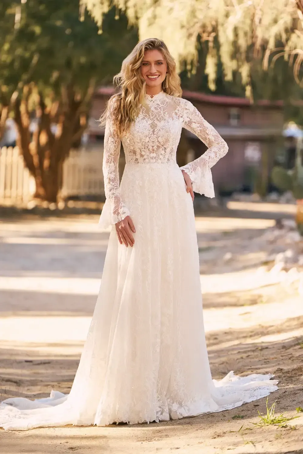 Woman in a white lace wedding dress, standing outdoors, smiling.