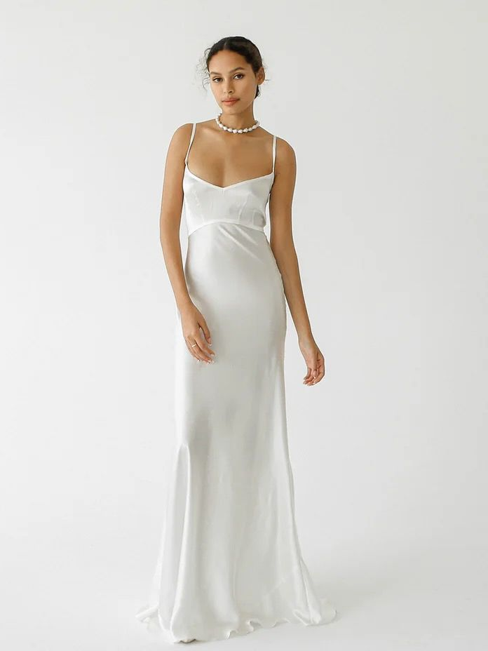 Woman in a white slip dress poses against a white background; wearing a pearl necklace.