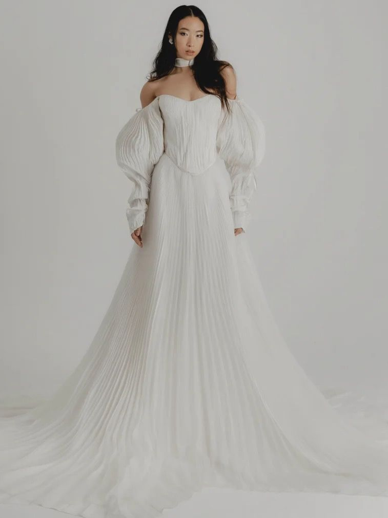 Woman in white off-the-shoulder wedding gown with long train, posing in a studio.