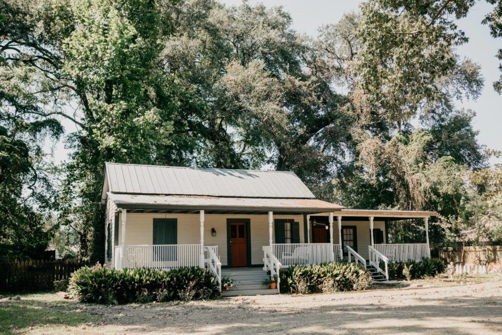 A white house with a porch and trees in the background.