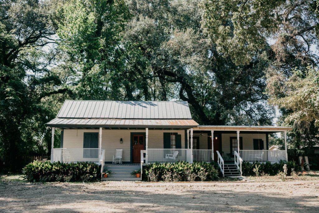 A white house with a porch is surrounded by trees.