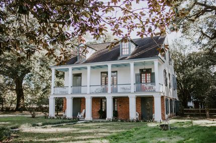 A large white house with a porch is surrounded by trees.
