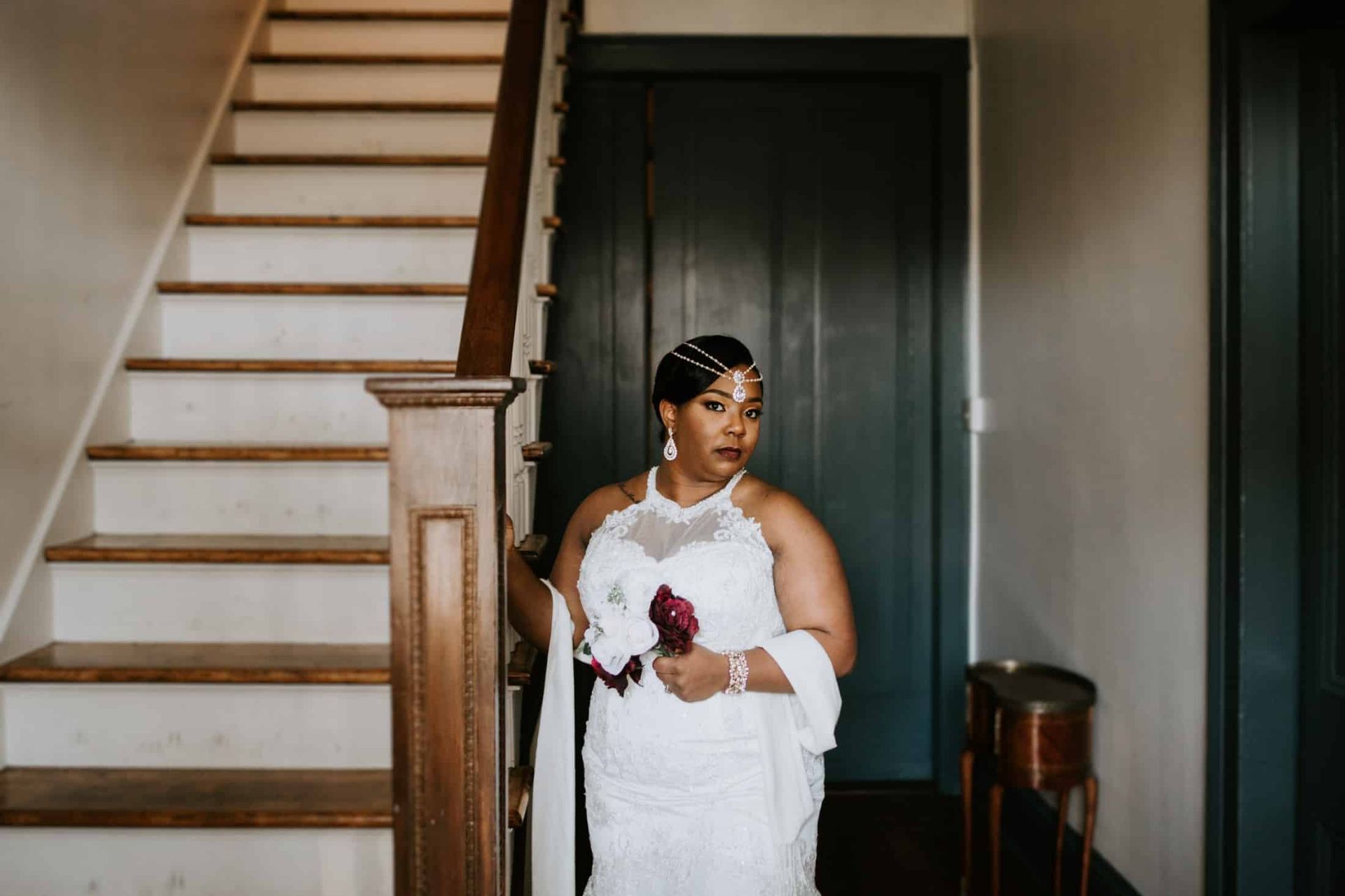 A bride in a white dress is standing on a set of stairs holding a bouquet of flowers.