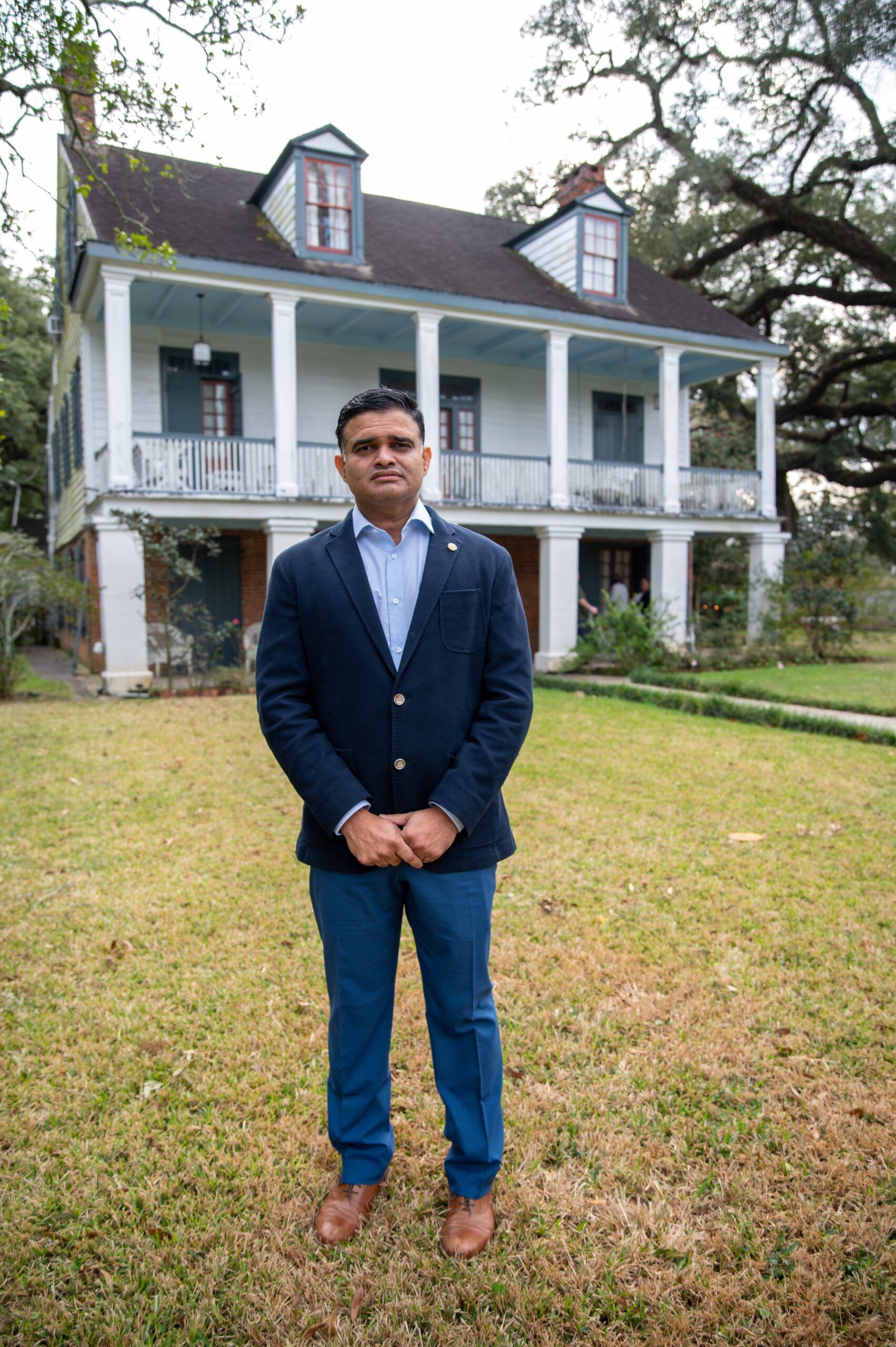 A man in a suit is standing in front of a large white house.