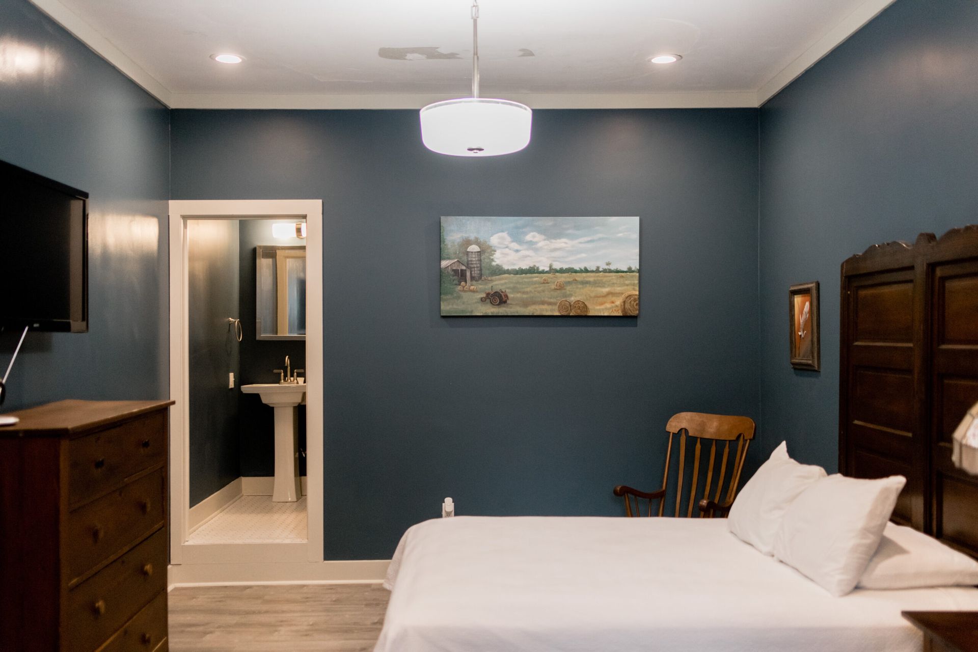 A bedroom with a bed , dresser , television , and a painting on the wall.