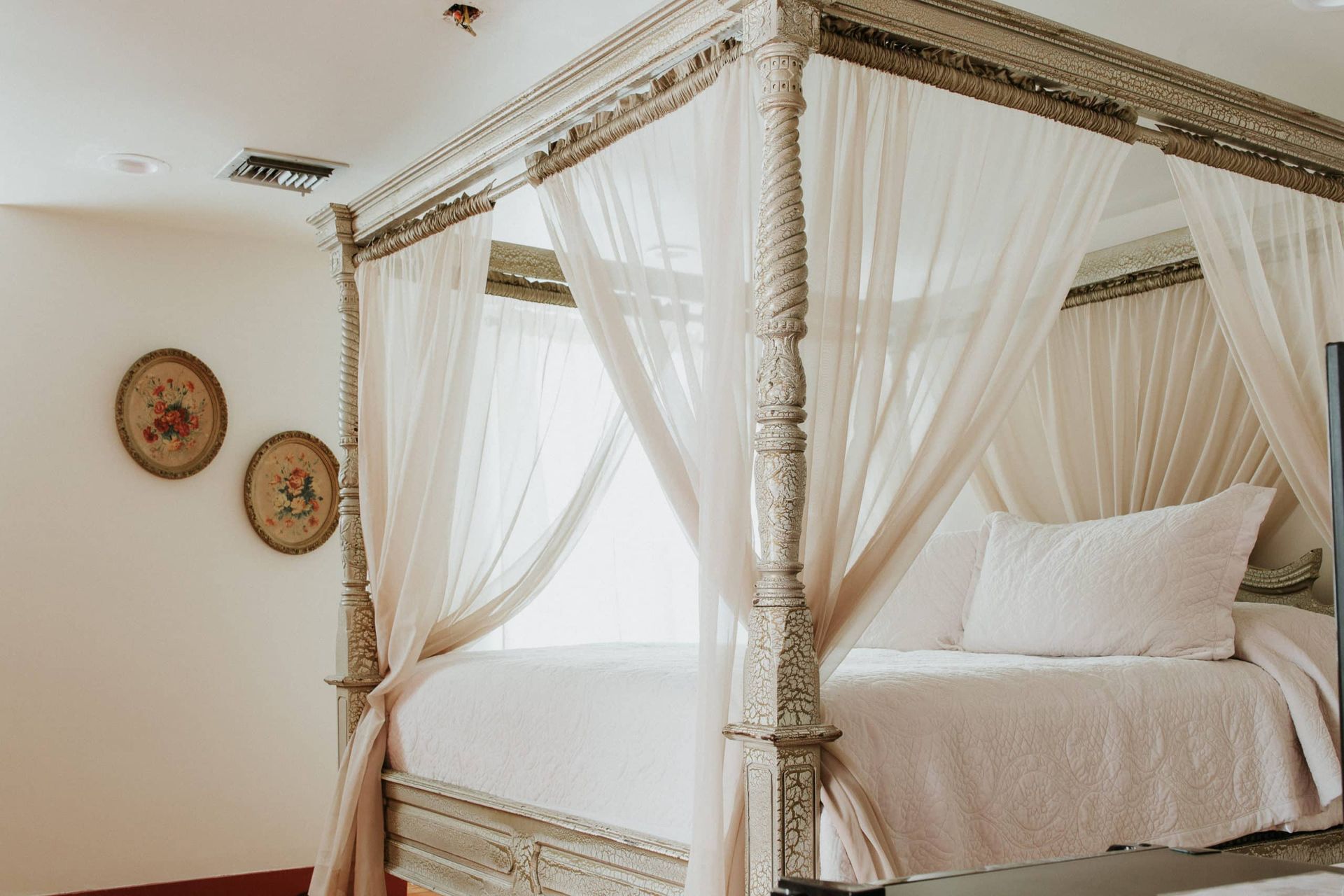 A four poster bed with white curtains in a bedroom.