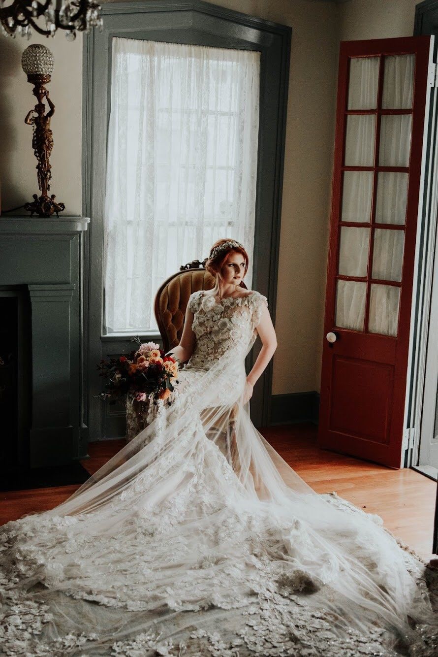 A bride in a long wedding dress is sitting in a chair in a room.