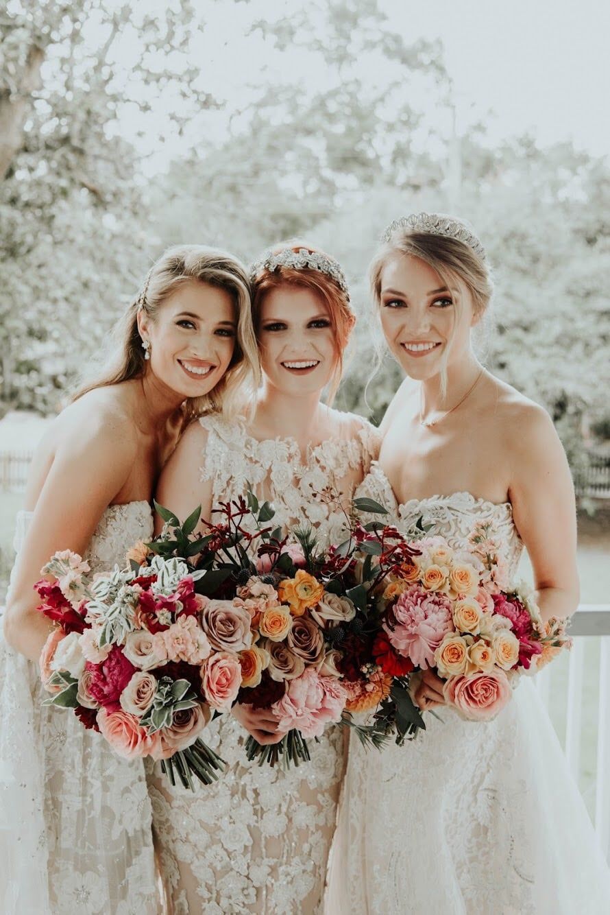 Three women in white dresses are posing for a picture while holding bouquets of flowers.