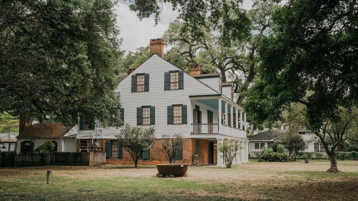 A large white house with black shutters is surrounded by trees and grass.