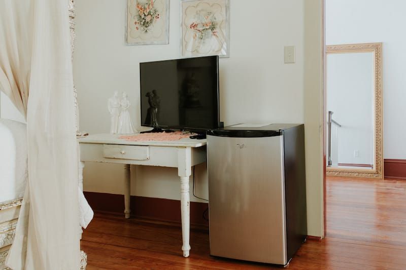 A room with a desk , refrigerator , television and mirror.