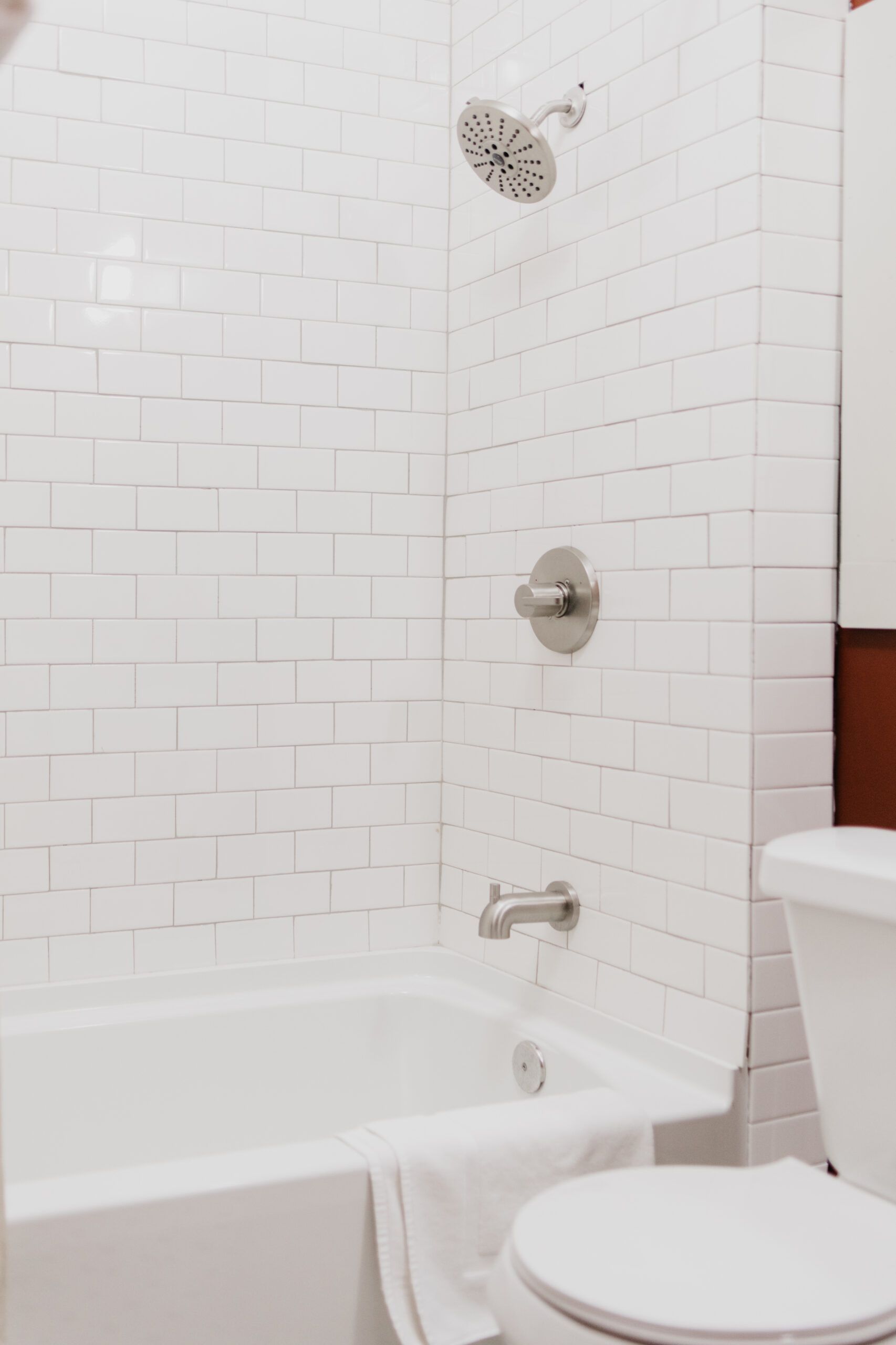 A bathroom with white brick walls , a tub , toilet and shower.