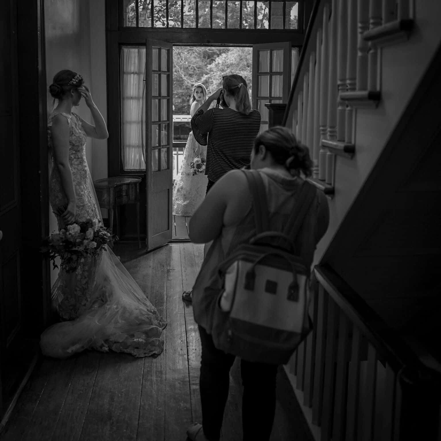 A black and white photo of a woman taking a picture of a bride in a wedding dress.