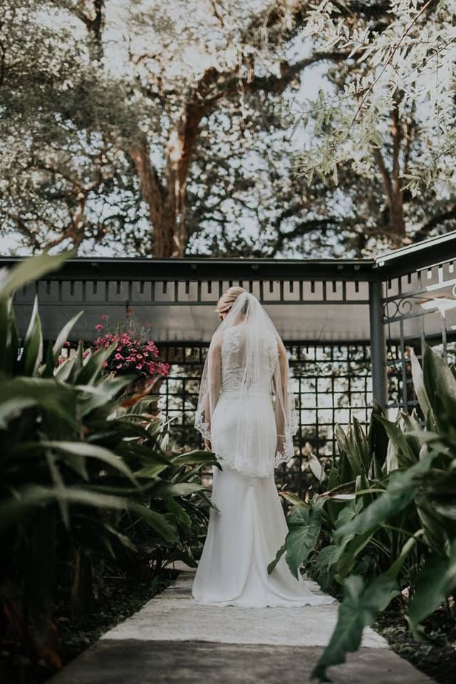 A bride in a wedding dress and veil is standing in a garden.