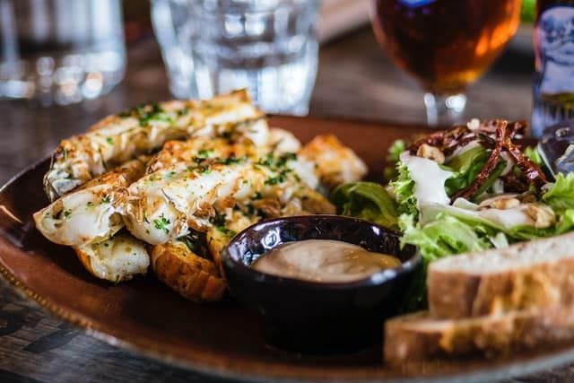 A close up of a plate of food on a table with a glass of beer in the background.