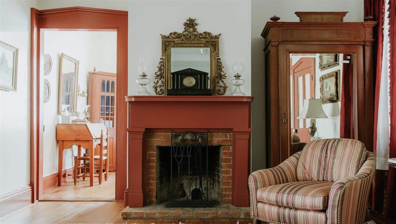 A living room with a fireplace , chair , mirror and clock.