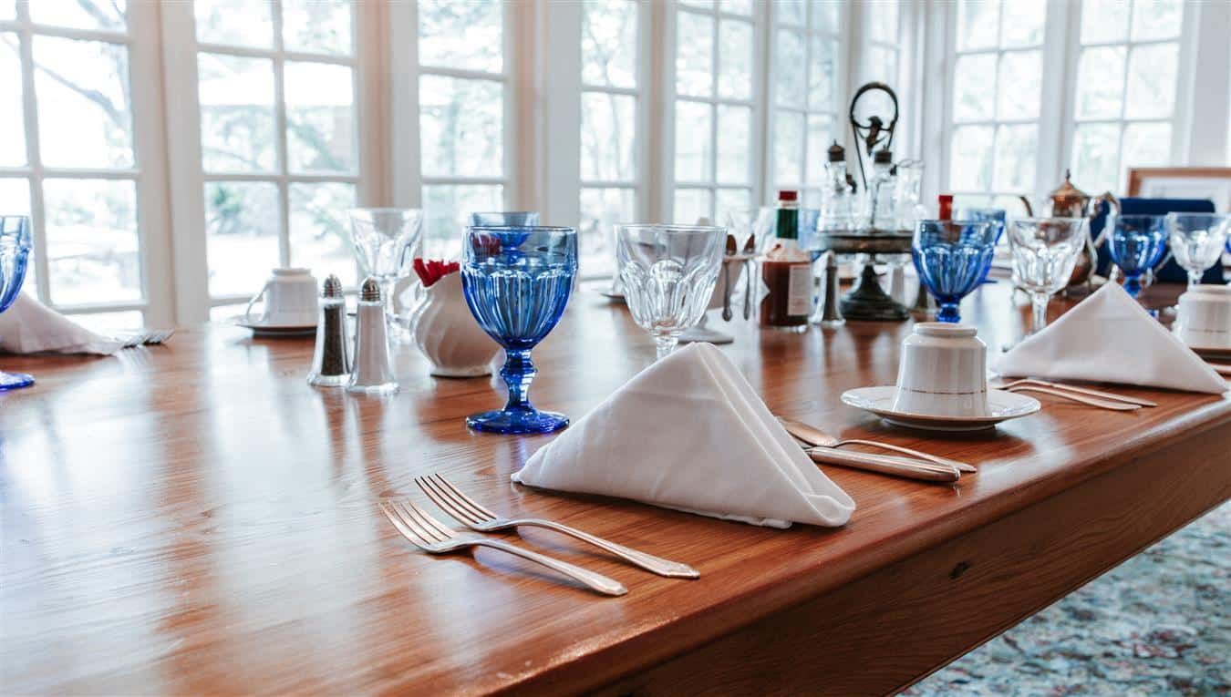 A long wooden table with blue glasses , silverware , and napkins.