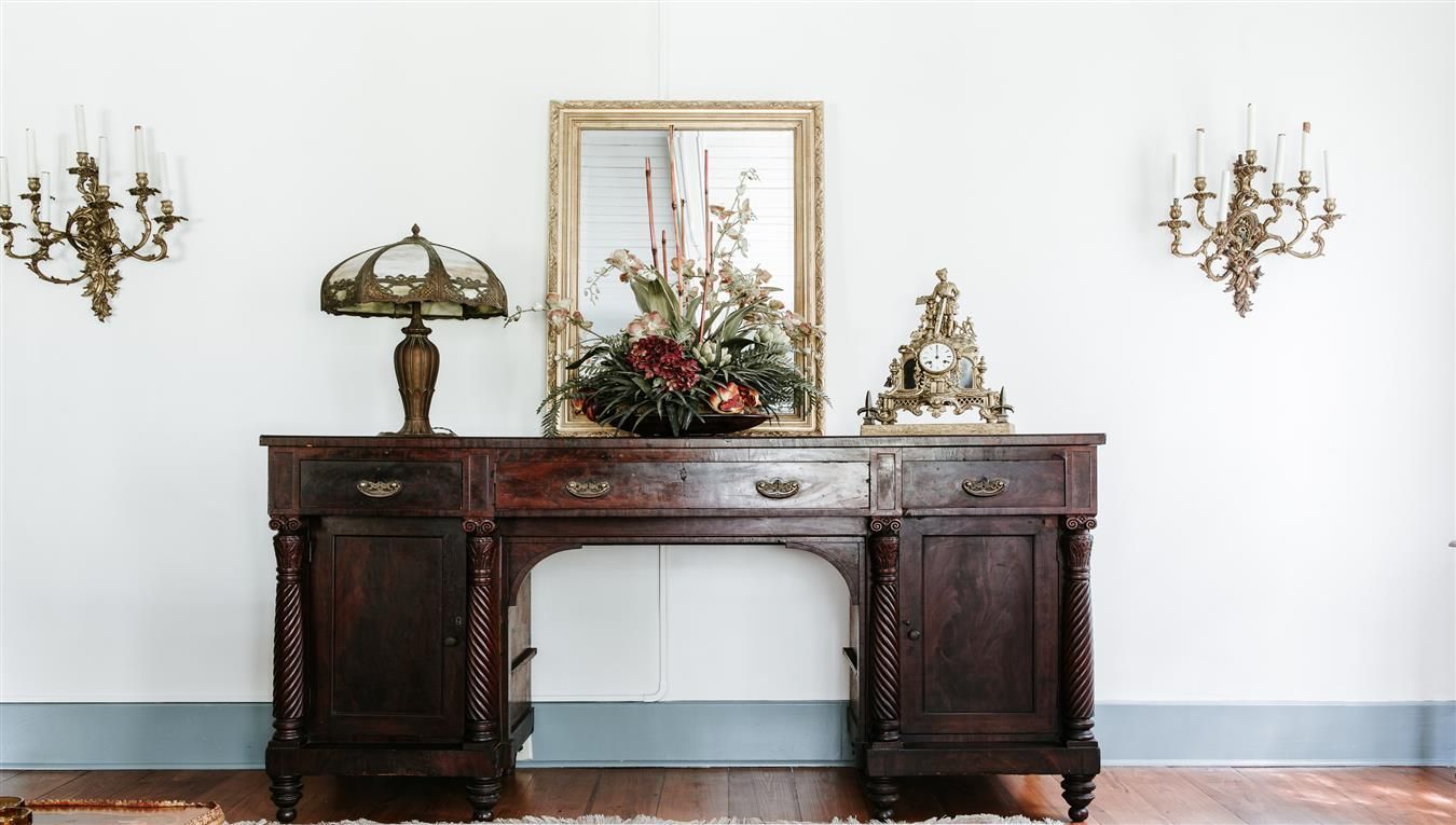 A wooden desk with a lamp , mirror and clock on it in a room.