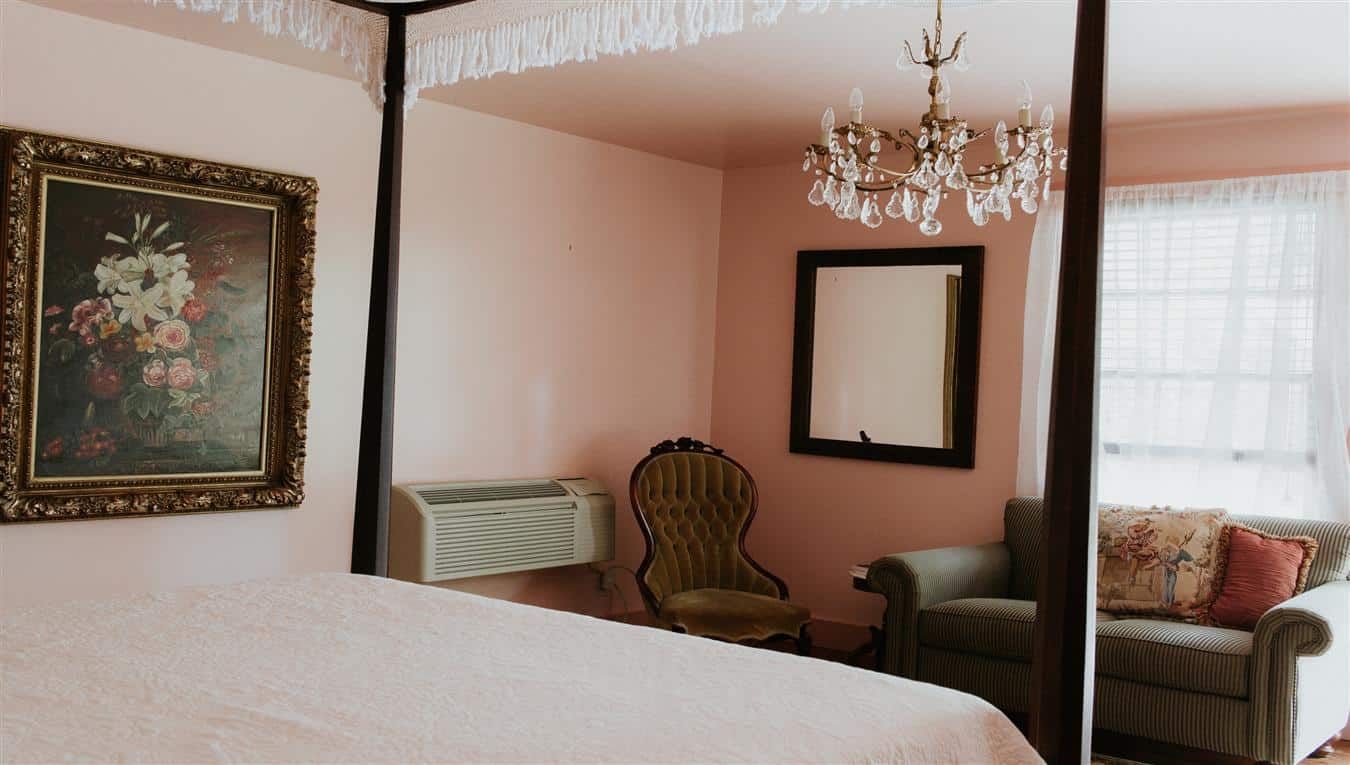 A bedroom with a four poster bed , couch , chair and mirror.