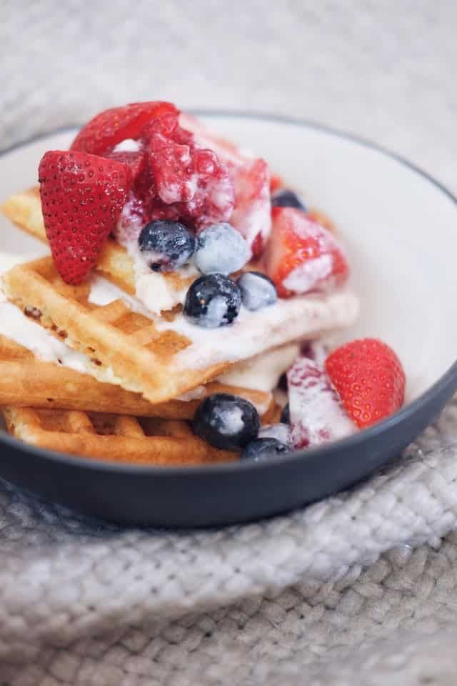 A bowl of waffles with strawberries and blueberries on top.