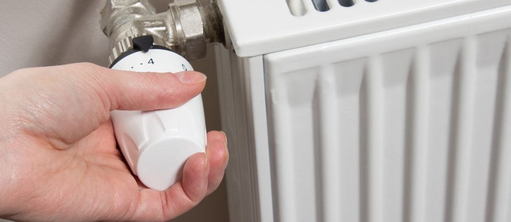 A hand adjusting a white radiator valve on a white radiator.