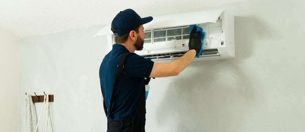 Person in uniform cleaning an air conditioner unit on a white wall.