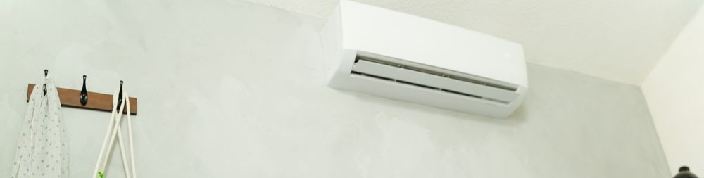 White air conditioner mounted on a white wall. Some items hanging on a wooden rack.