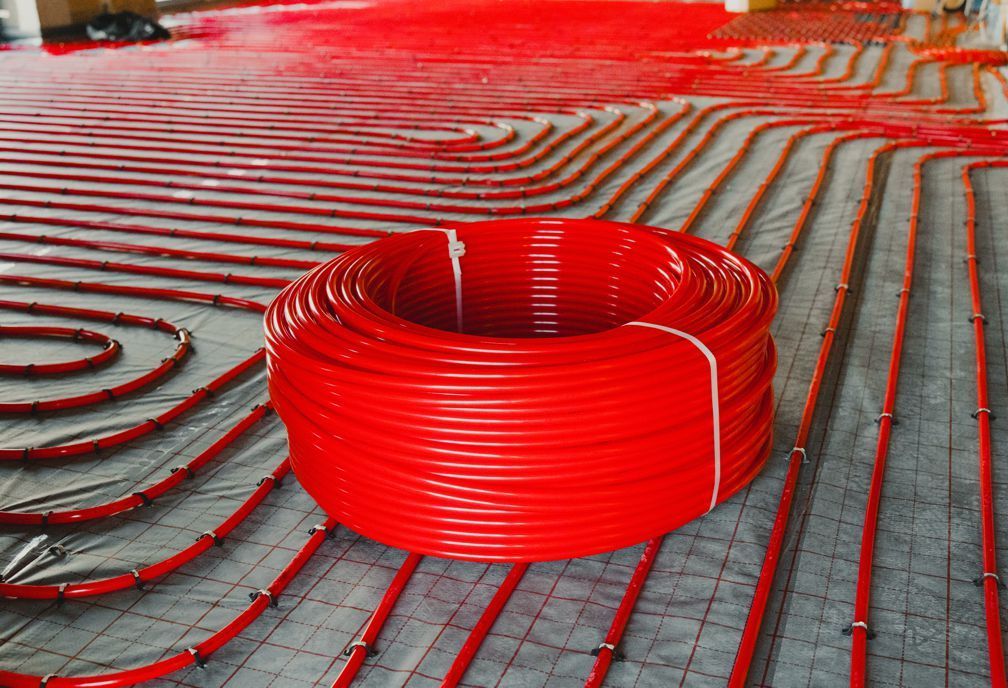 Red radiant floor heating tubes coiled and installed on a gray concrete floor.