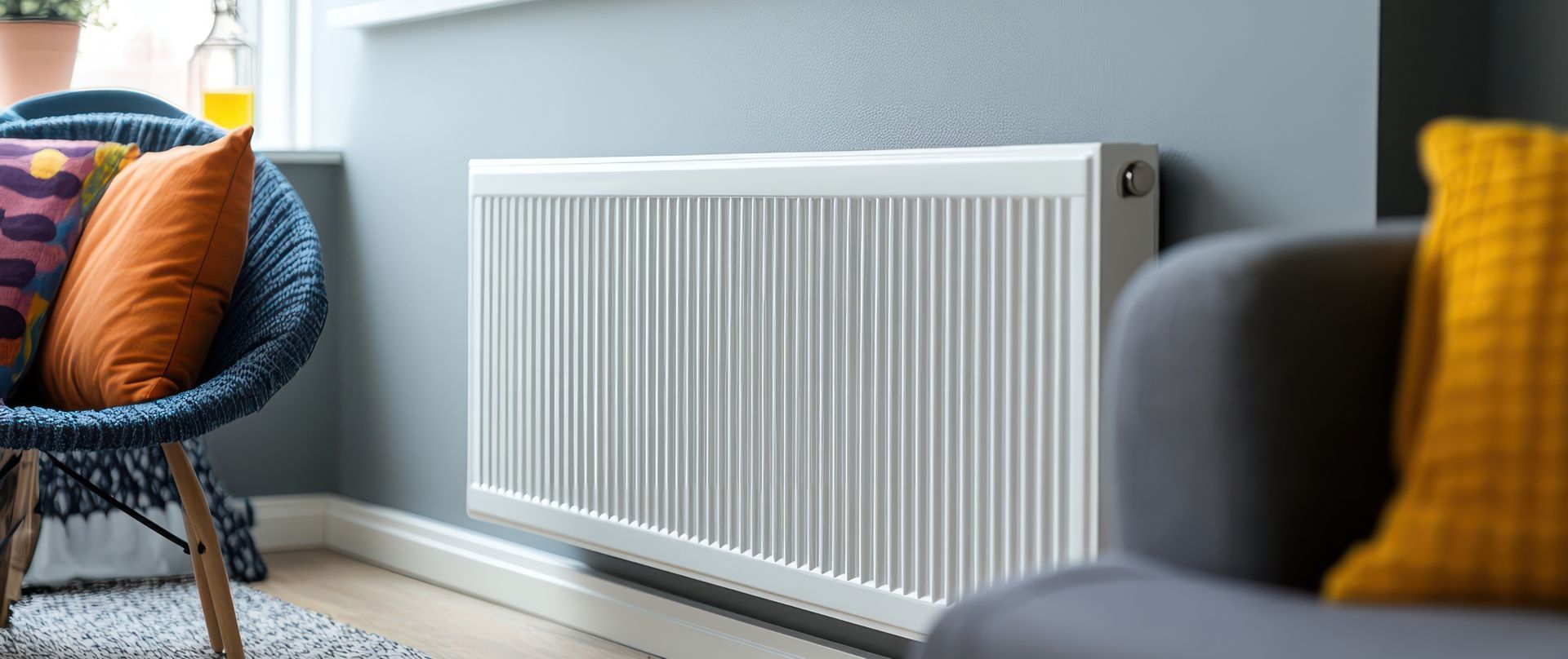 White radiator on a blue wall in a living room, with a blue chair and gray couch.
