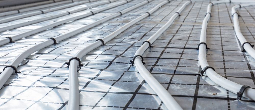 Pipes installed for underfloor heating, secured to a grid on the floor.
