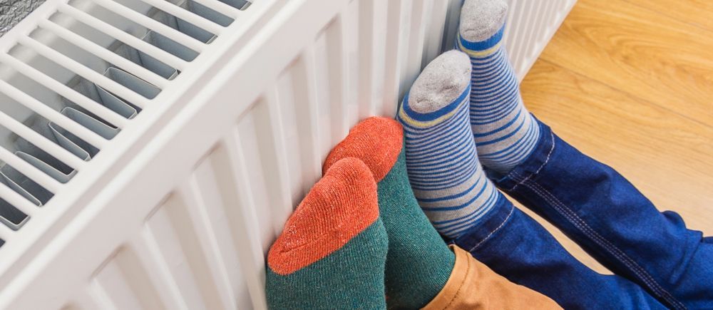 Feet in colorful socks resting on a white radiator against a wood floor.
