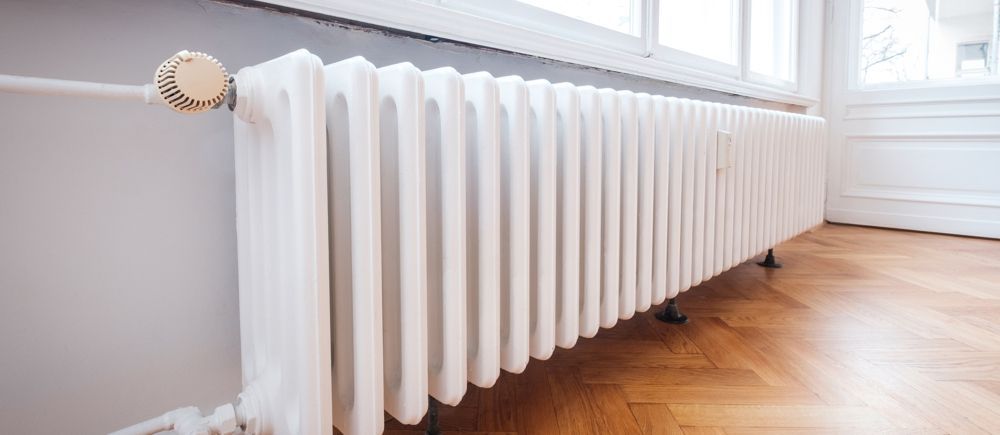 White radiator in a room with hardwood floors and a window.
