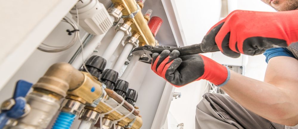 Plumber in red gloves using a wrench to work on plumbing pipes.