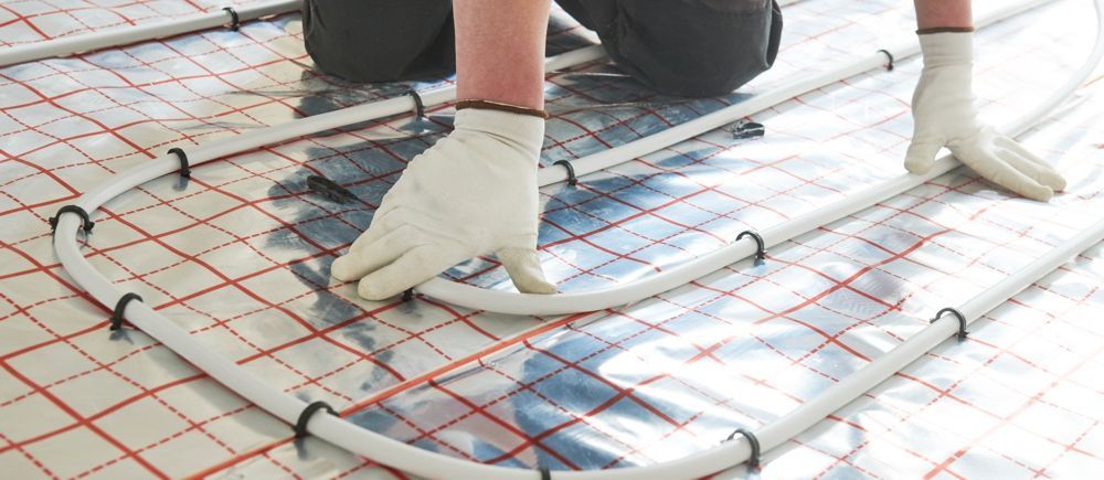 Person installing radiant floor heating tubes on a grid-patterned insulation sheet.