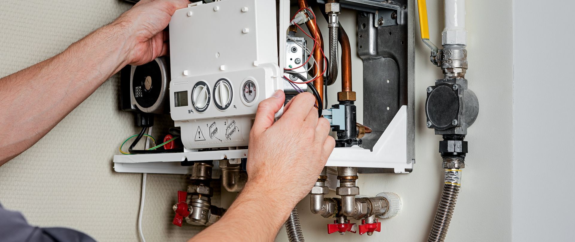 A person is repairing a water heater, working with wires and pipes attached to the unit.